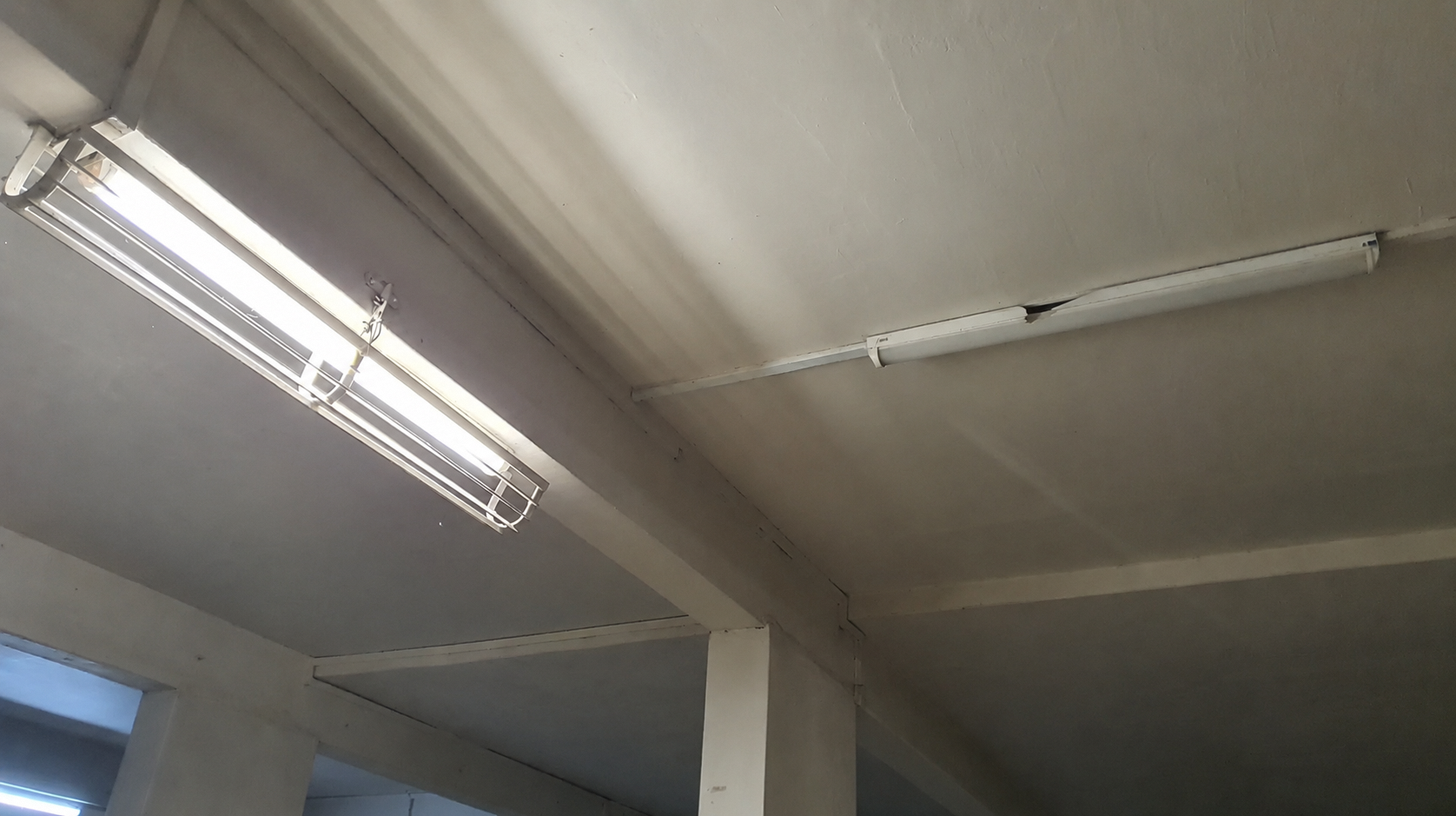 A ceiling with two tube lights — one lit and working, the other dark with a broken casing.